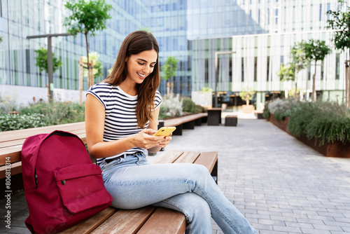 Smiling hispanic woman using online app. Student girl using cell phone outdoors at University campus 