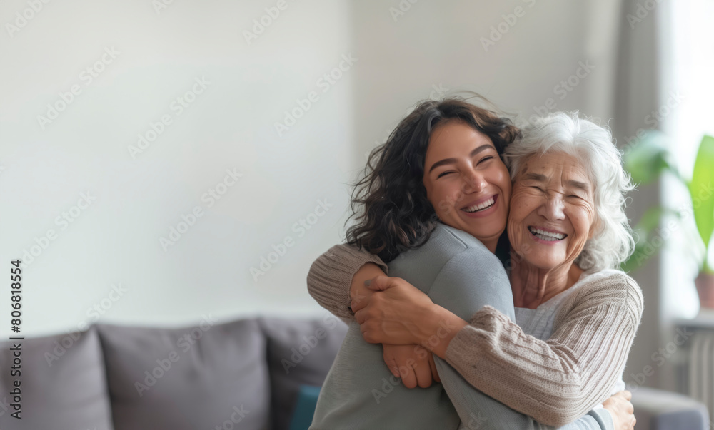 Two women hug each other in a living room. One woman is smiling and the other is also smiling. Scene is warm and friendly,Joyful Bonds: Embracing Generations in the Heart of Home