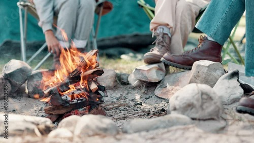 Wood, fire and legs with camping on people in nature for vacation, heat and comfort on holiday. Friends, rocks and campfire with flame with smoke on ground for travel, adventure and warm in forest photo