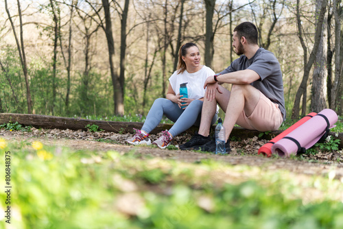 Sitting on a fallen tree trunk, the couple, including the determined overweight female, catch their breath, their laughter blending with the rustling leaves as they enjoy a post-workout moment. 