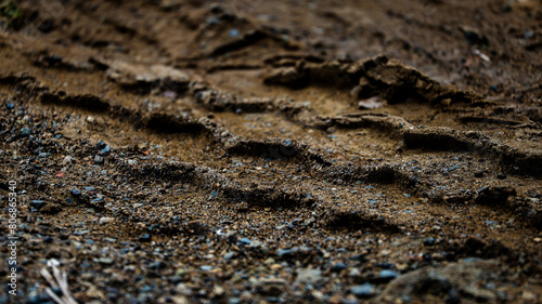 Closeup of wheel track or tire track on soft wet ground or soil. Vehicle wheel tracks in mud, soil, ground texture. Road construction site backdrop. Heavy machinery imprint.