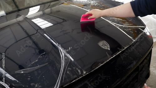 Close up of paint protection film installation on front bumper of modern luxury car. PPF is polyurethane film applied to car surface to protect the paint from stone chips, bug splatter, and abrasion.	