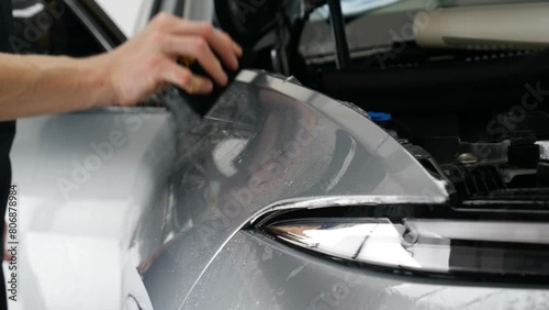 Close up of paint protection film installation on front bumper of modern luxury car. PPF is polyurethane film applied to car surface to protect the paint from stone chips, bug splatter, and abrasion.