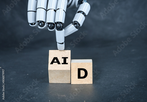 Robot hand turns cube and puts the letter 'AI' in to the word 'aid'. Symbol that artificial intelligence technology is helping.