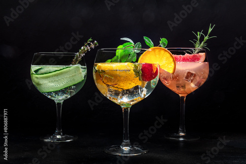 Fancy cocktails with fresh fruit. Gin and tonic drinks with ice at a party, on a black background. Alcohol with cucumber, orange, rosemary, mint