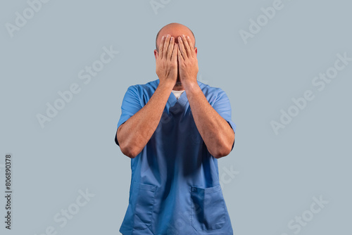 Portrait of a female physiotherapist wearing light blue dress and hands covering her face.