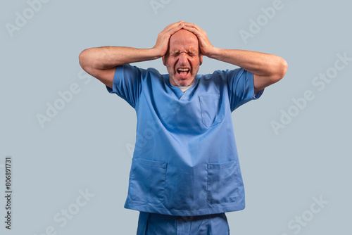 Portrait of a physiotherapist in light blue gown and hands on head.