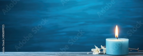 Blue background with white thin wax candle with a small lit flame for funeral grief death dead sad emotion with copy space texture for display  photo