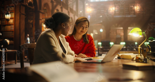 Engaged Multiethnic Students Studying Together in a Classic Library. Asian and African American Women Focused on Learning with Laptop and Books  Preparing for University Exams.