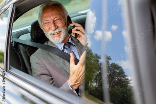 Elegant senior businessman chatting on phone while riding in a luxury car