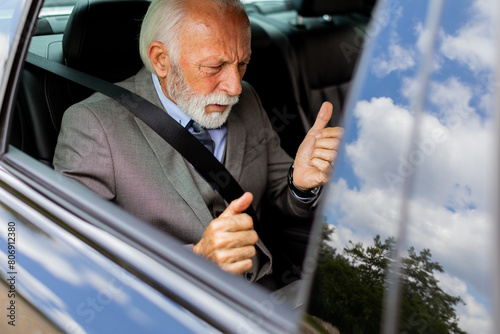 Senior businessman working on laptop while riding in backseat of car