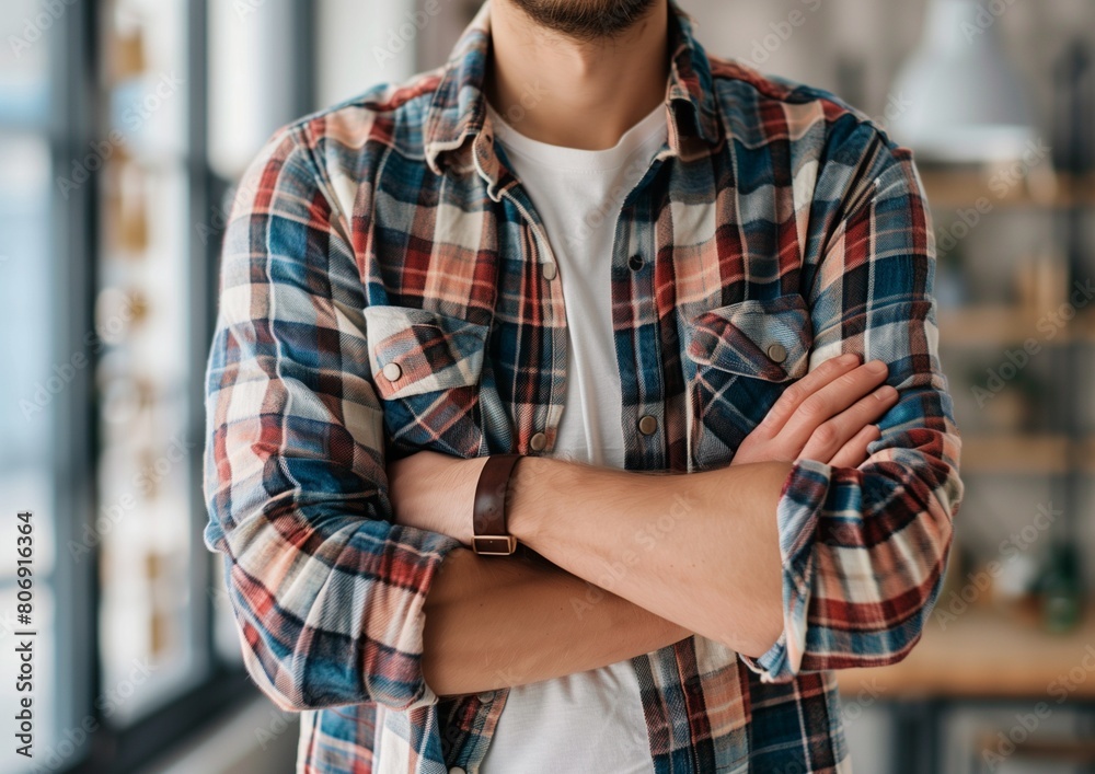 Obraz premium Confident Young Man Standing with Arms Crossed Wearing Plaid Shirt in Modern Office