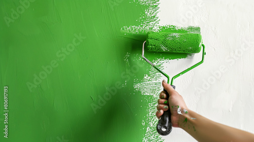 Close-up image of a hand using a green paint roller on a white wall, mid-process. photo