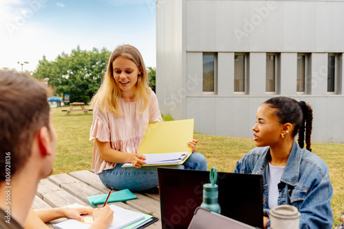 multiracial group of students with focus on young white girl studying together seated at a table outside the college campus