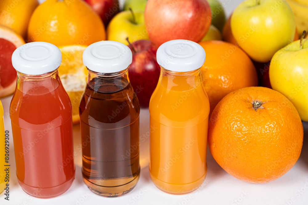 Assortment of fruit juices in glass bottles among fruits on white background Assortment of fruit juices in glass bottles among fruits on white background