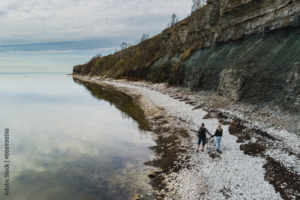 A young couple walks hand in hand along the seashore near the Paldiski cliff on a spring day.