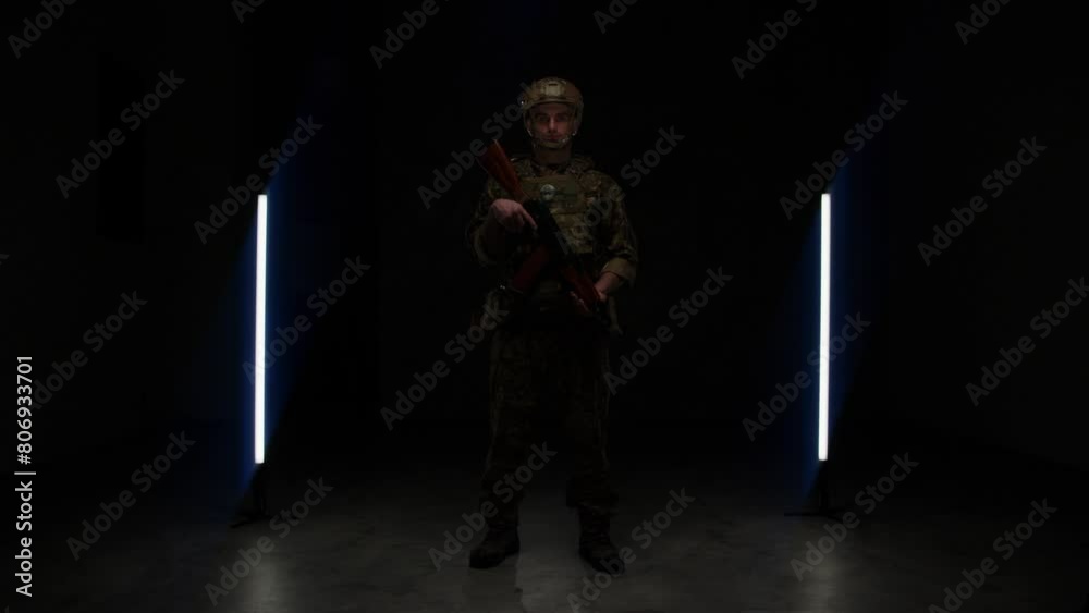 military man in ammunition with a weapon in his hands in a dark room on the background of a black wall. general plan a special officer military man in ammunition with a weapon in his hands in a dark room on the background of a black wall. general plan a special officer