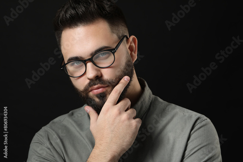 Young man with mustache touching face on black background