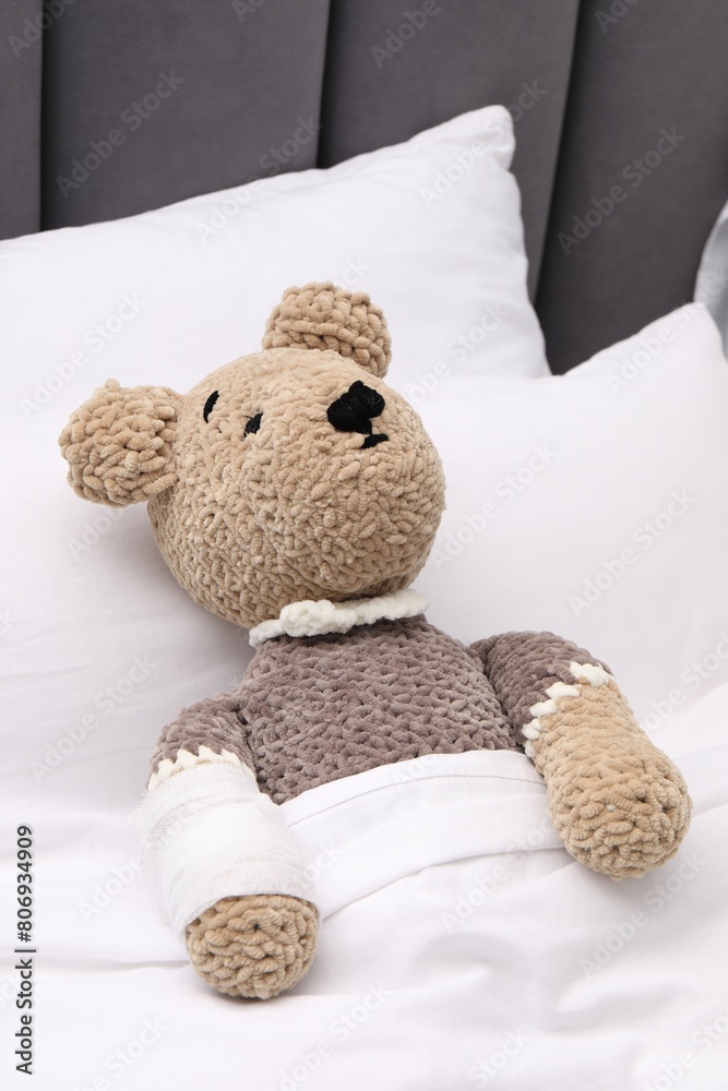Toy cute bear with bandage under blanket in bed