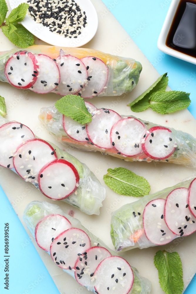 Delicious spring rolls, mint, sesame and soy sauce on light blue background, top view Delicious spring rolls, mint, sesame and soy sauce on light blue background, top view