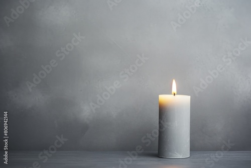 Gray background with white thin wax candle with a small lit flame for funeral grief death dead sad emotion with copy space texture for display 