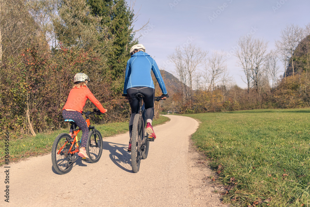 Naklejka premium Mother and daughter, little girl, riding bikes along a scenic rural landscape. Outdoors family activity concept.