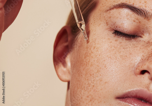 Close-up highly detailed shot of female skin with freckles and pipette with serum. Cropped shot of young woman with smooth perfect skin applying liquid serum on face. photo