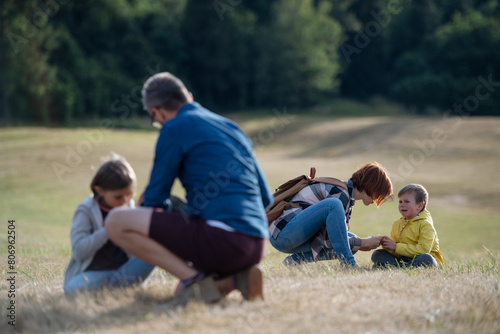 Teacher helping injured boy after fall. Young students running across meadow during field teaching class. Dedicated teachers during outdoor active education.