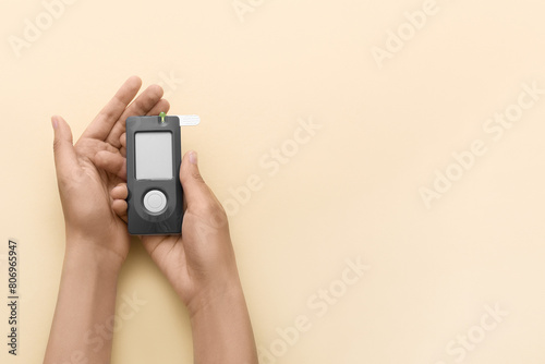 Glucometer in hands on a beige background. Top view. Space for text.