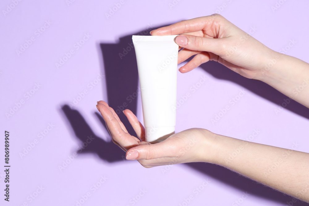Woman holding tube of cream on violet background, closeup Woman holding tube of cream on violet background, closeup