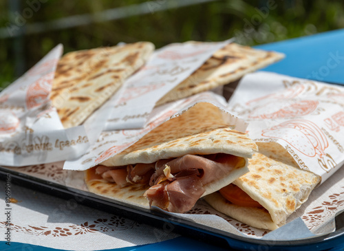 Two Piadina Romagnola Wrapped in unbranded but decorated oily paper, authentic street food from the Riviera Romagnola region of Italy, stacked one on top of the other. Prosciutto Crudo ham filling. 