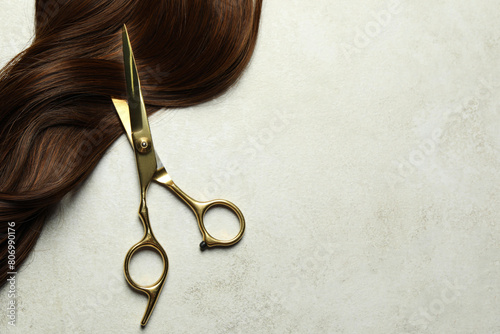 Obraz na plátně Professional hairdresser scissors with brown hair strand on grey table, top view