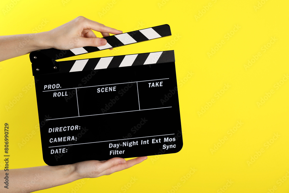 Woman holding movie clapper on yellow background, closeup. Space for text
