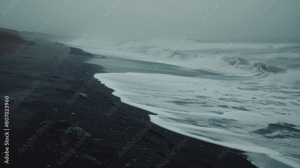   A large body of water rests atop a black sand beach, teeming with numerous waves
