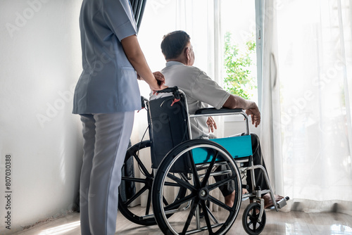 Asian nurse caring for senior patient in a wheelchair. Nurse helping senior man in nursing home