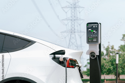 Electric vehicle or EV car recharge battery at charging station connected to power grid tower electrical industrial facility as electrical industry for eco friendly vehicle utilization. Expedient photo