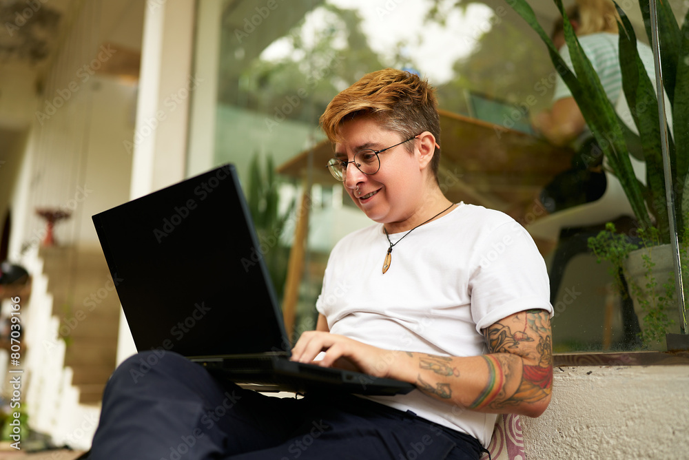 custom made wallpaper toronto digitalTattooed Gen Z transgender person works on laptop in cozy office space, displays casual, inclusive workspace. Focused yet comfortable, represents modern work-life balance, LGBTQ-friendly environment.