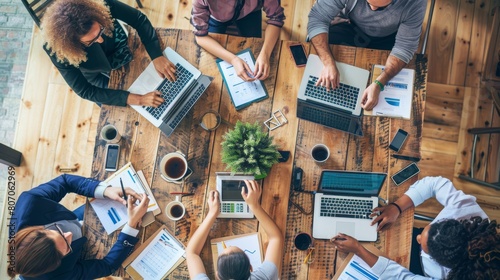 A group of people are sitting around a table with laptops and papers