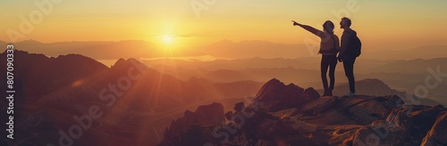 silhouettes of a couple pointing at a sunset in mountains, a panoramic view with for a travel and adventure concept photo