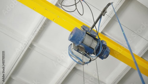 Overhead view of electric hoist on a yellow beam in an industrial workshop. Crane cathead for lifting and moving materials in factory, warehouse. 