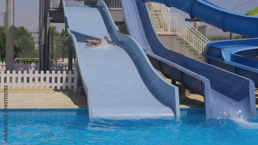 Boy slides down a water slide into a sparkling pool with joy