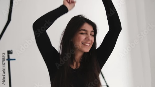 A young happy dark-haired woman is dancing in a photo studio.The woman touches her fluttering hair with her hands.