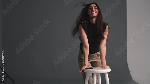 A young happy dark-haired woman is dancing in a photo studio.The woman touches her fluttering hair with her hands.