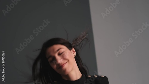 A young happy dark-haired woman is dancing in a photo studio.The woman touches her fluttering hair with her hands.