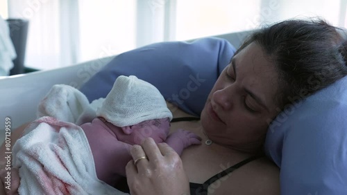 Mother holding newborn baby right after giving birth, first seconds of life of an infant resting on mother's chest emphasizing skin to skin contact, mom struggling with pain during joyful moment photo