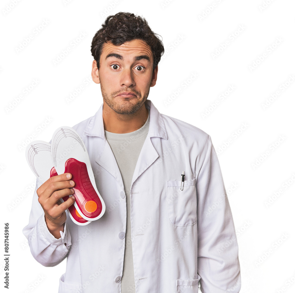 Young Hispanic podiatrist with insoles shrugs shoulders and open eyes confused. Young Hispanic podiatrist with insoles shrugs shoulders and open eyes confused.
