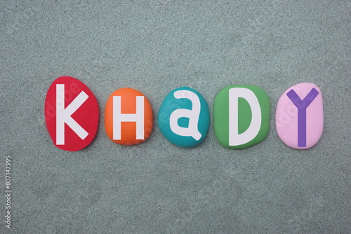 Celebration of Khady, feminine given name composed with multi colored stone letters over green sand