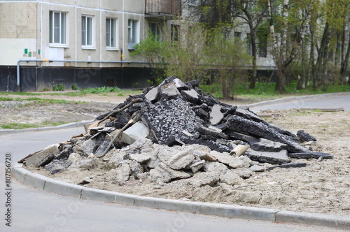 A pile of broken asphalt lies near the wall of an apartment building