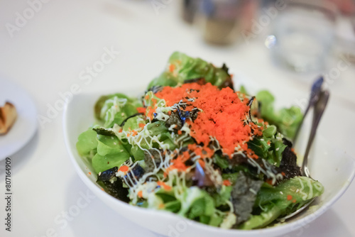 Green vegan salad from green leaves mix and vegetables, top view on white table. Green salad, close up by green vegetable, seaweed, and tobiko dressing on a white plate, isolated on white background.