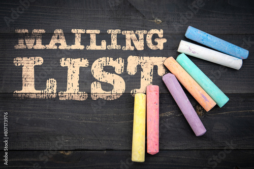 Mailing List. Text and pieces of chalk on a dark wood texture background